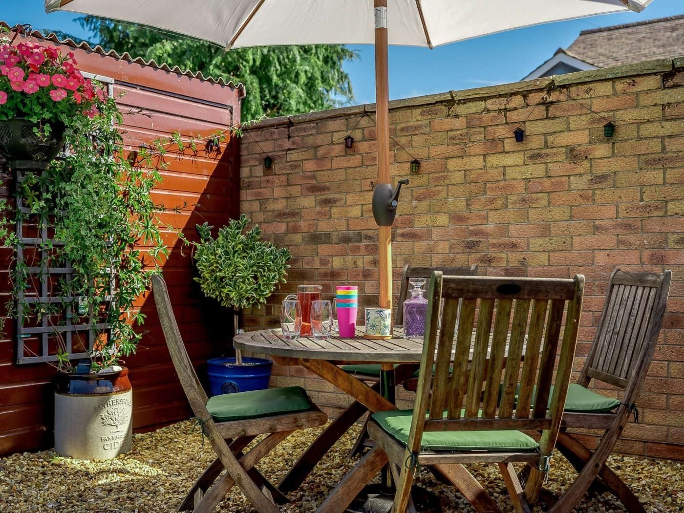 An outdoor patio with a round table, two wooden chairs, a potted plant, and a brick wall.