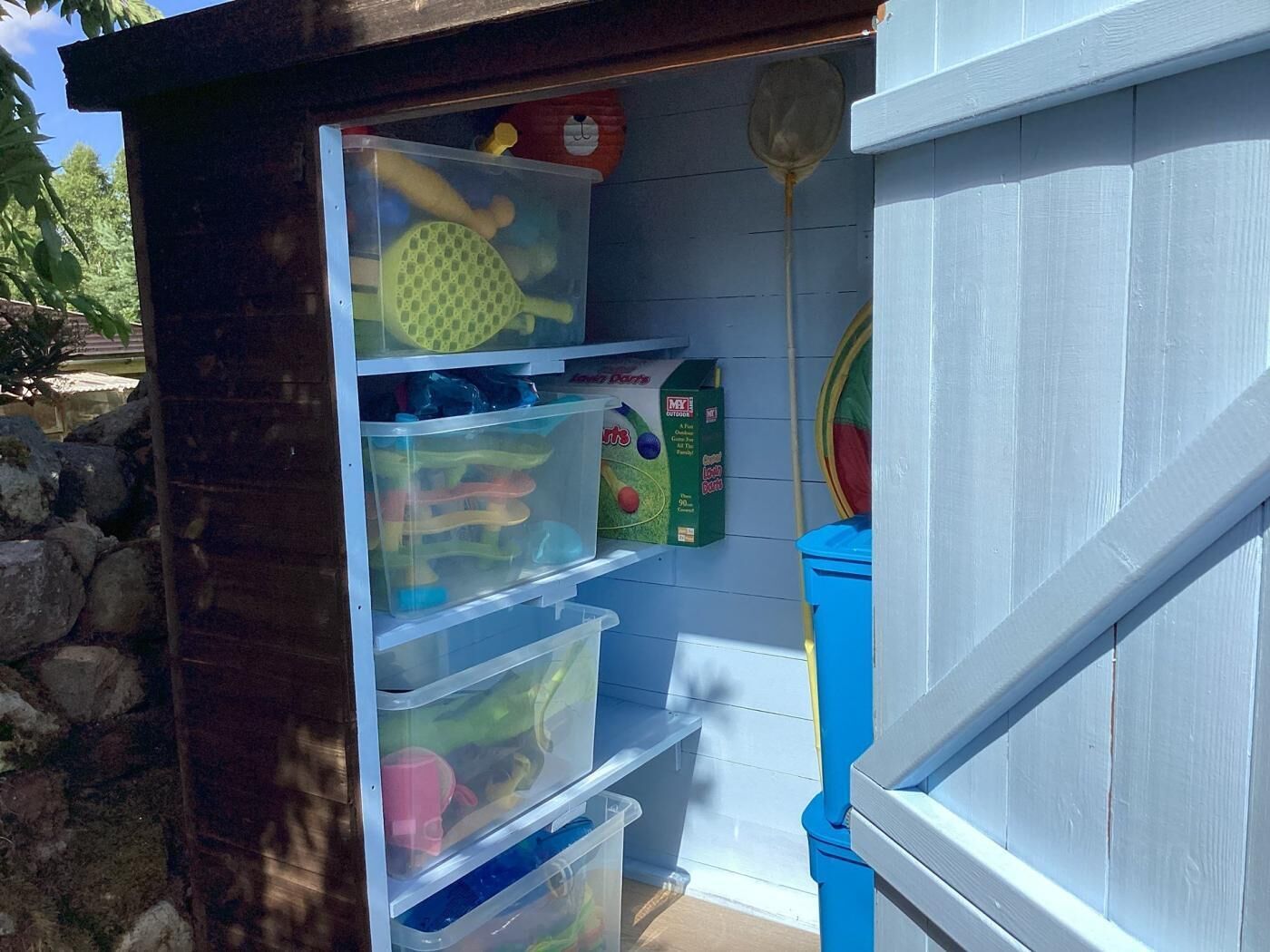 A storage unit with multiple transparent plastic bins, a toy box, and a hanging net.