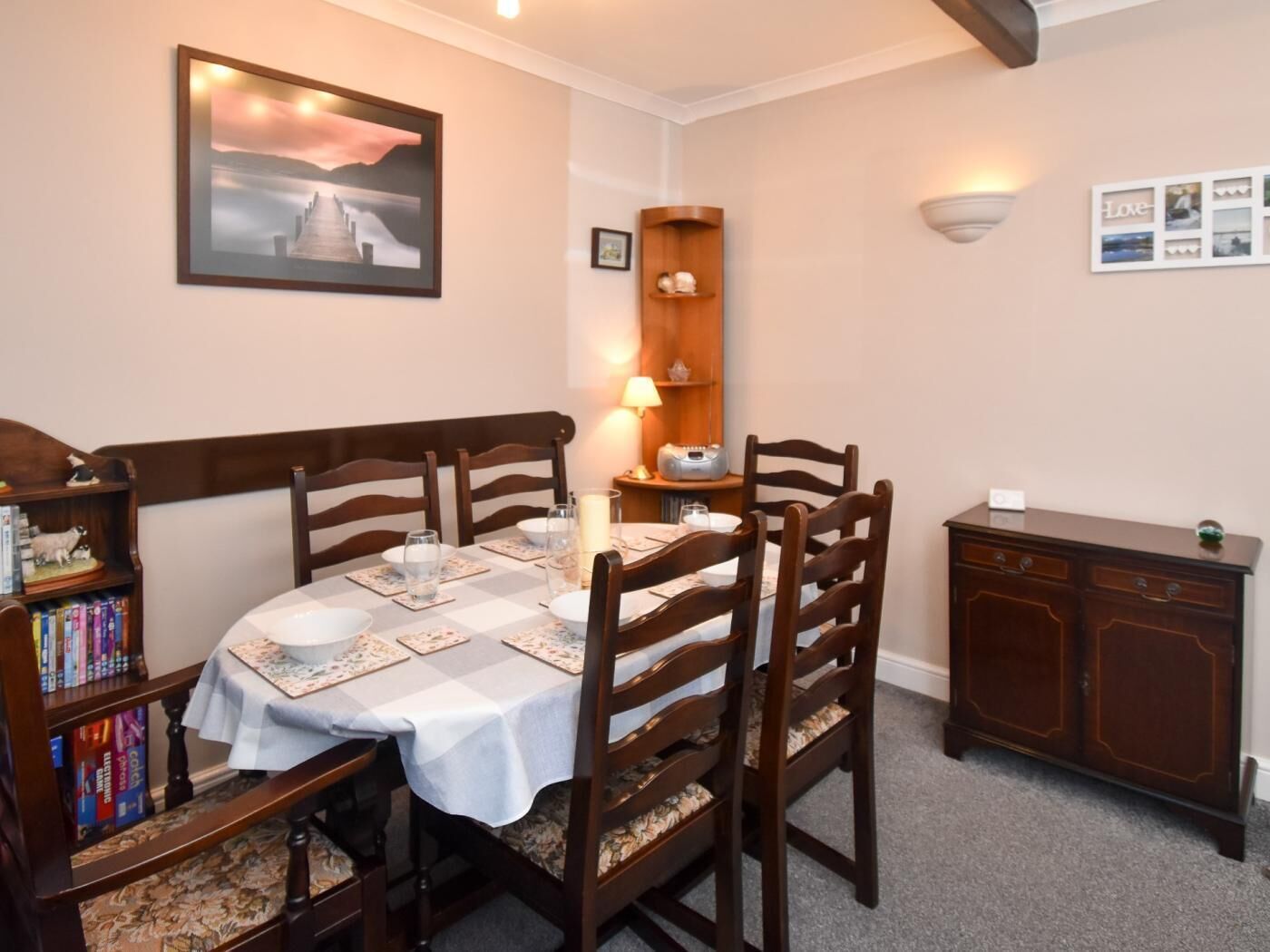 A dining area with a table set for four, surrounded by wooden chairs, a bookshelf, a cabinet, and a framed picture on the wall.