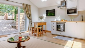 A modern kitchen with a TV, a dining area with a table and chairs, and a view through a glass door. - 1 Bed in Matlock (oc-89283) (Stanton Lees)