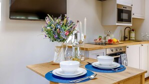 A modern kitchen with a flat-screen TV, a gas stove, and a dining area set with white plates and bowls. - 1 Bed in Matlock (oc-89283) (Stanton Lees)