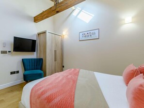 Ein Schlafzimmer mit einem Bett, einem blauen Sessel, einem Kleiderschrank, einem Fernseher und einer Wandleuchte.