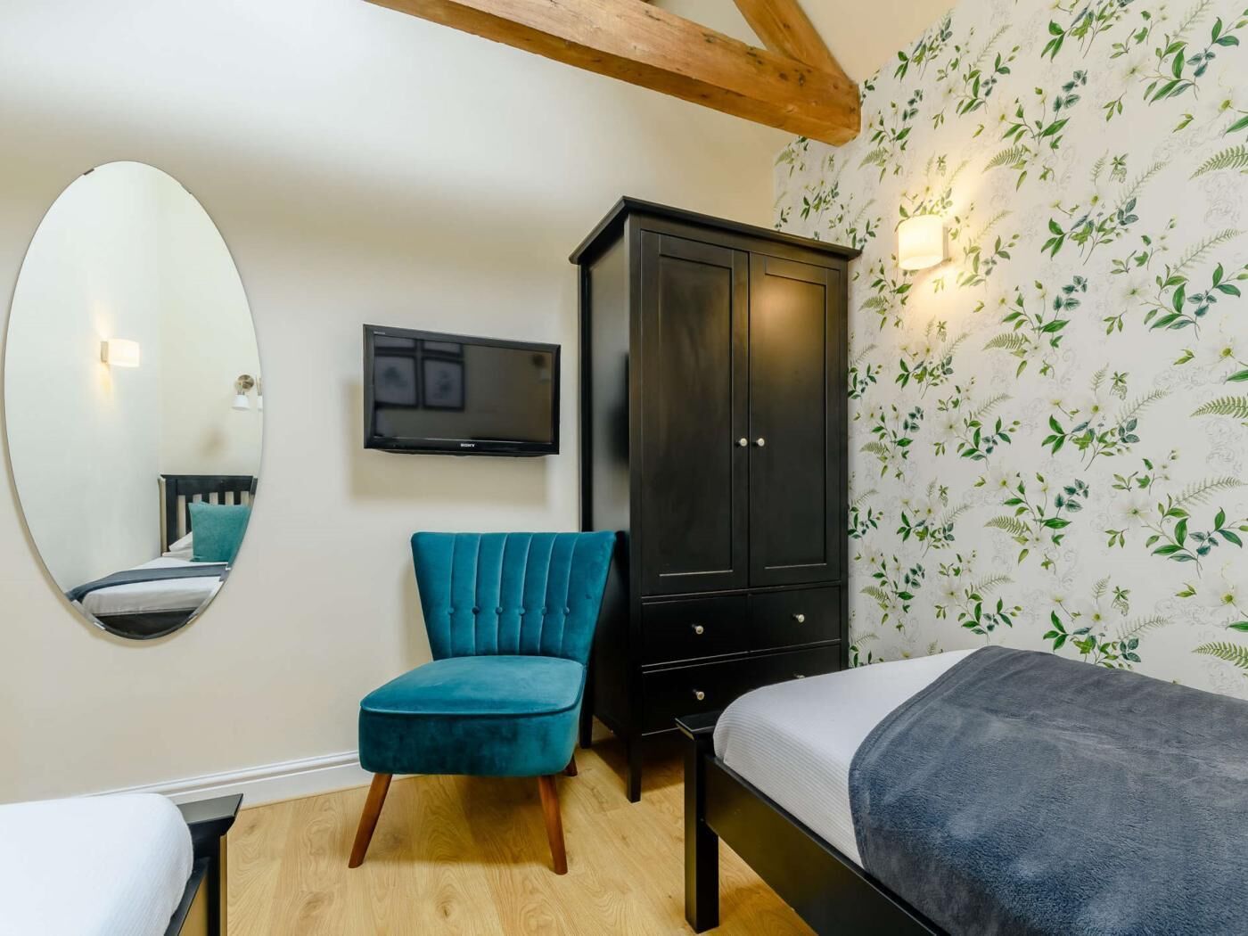 A bedroom with a bed, a chair, a wardrobe, a television, and a mirror.