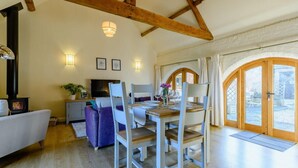 A cozy room with a wooden ceiling, a dining table with chairs, a sofa, a TV, and a fireplace. - 1 Bed in Evesham (oc-89306) (Church Lench)