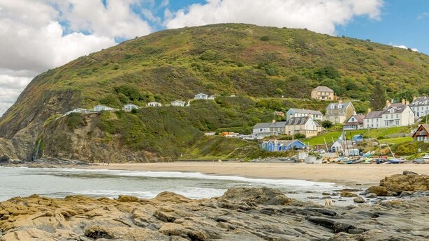 Un pueblo costero con casas en una ladera, playa rocosa y cielo despejado.