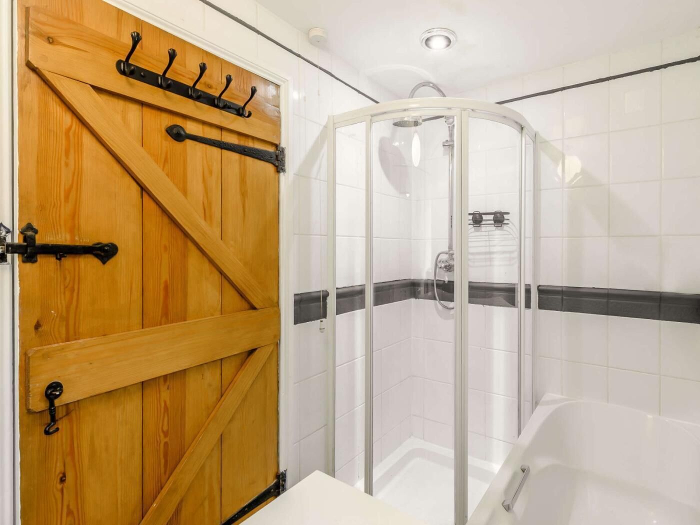 Een badkamer met een houten deur, een douchecabine van glas en een wit bad.