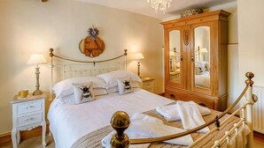 Een slaapkamer met een bed, nachtlampen, een houten kledingkast, een kroonluchter en een spiegel aan de muur.