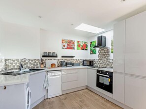 A modern kitchen with white cabinets, a dishwasher, a microwave, and a stove. There are three wall-mounted pictures of fruits and a ceiling light. - 2 Bed in Axminster (oc-89471) (Tytherleigh)