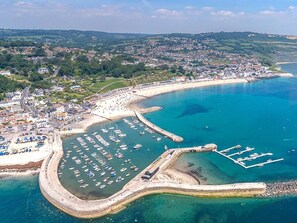 An aerial view of a coastal town with a marina, sandy beach, and surrounding greenery. - 2 Bed in Axminster (oc-89471) (Tytherleigh)