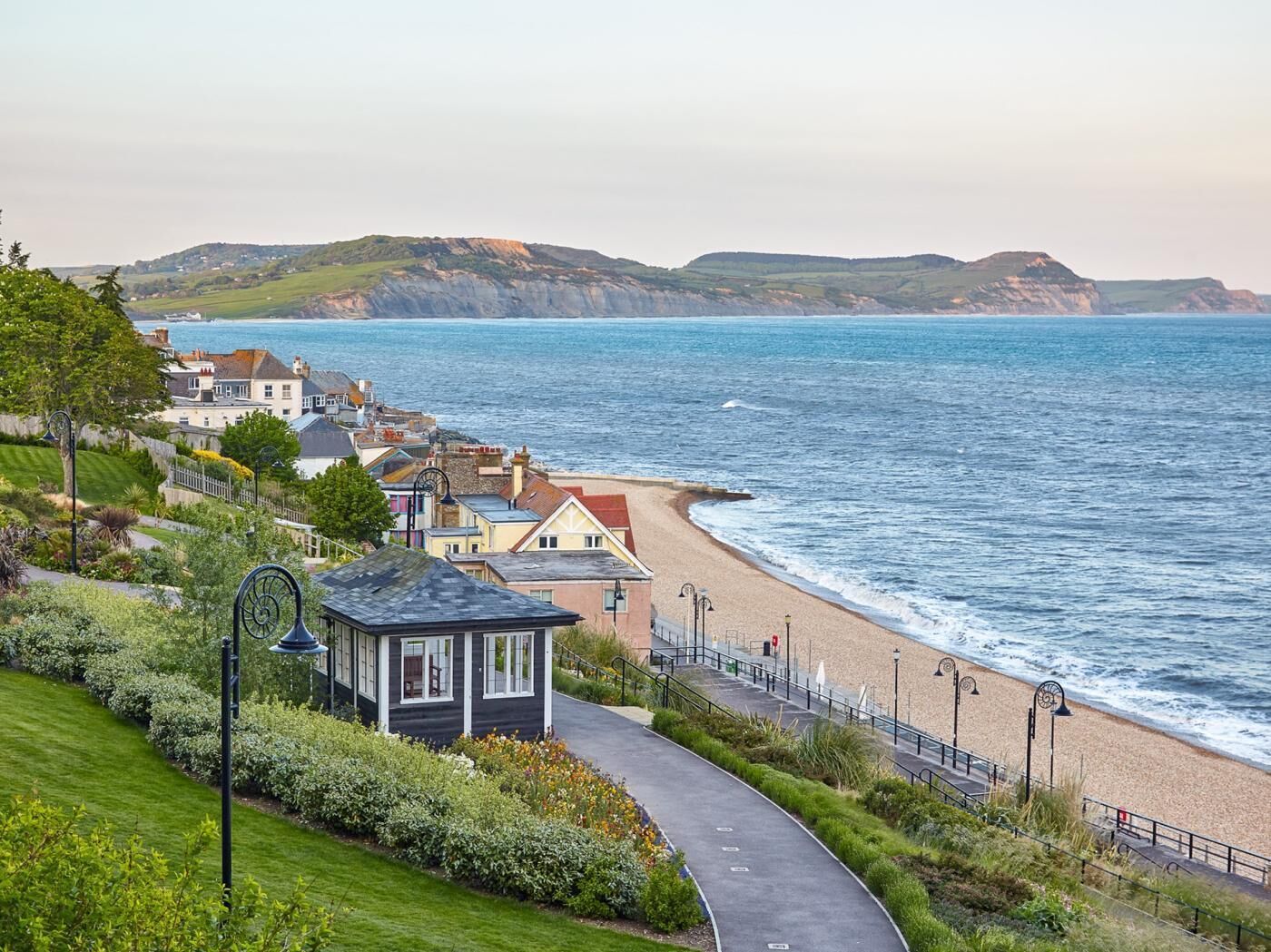 A coastal property with a paved walkway, a small structure, and a view of the sea and hills.