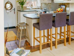 A kitchen with a central island, bar stools, a vase with flowers, and a fruit bowl.