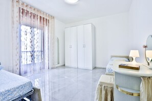 Une chambre d’hôtel avec un lit, une table de chevet avec une lampe, une armoire et une fenêtre avec des rideaux légers.