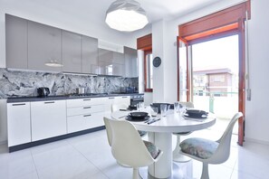 Une cuisine moderne avec des meubles blancs, un pare-feu en marbre et un coin repas comprenant une table ronde et des chaises.