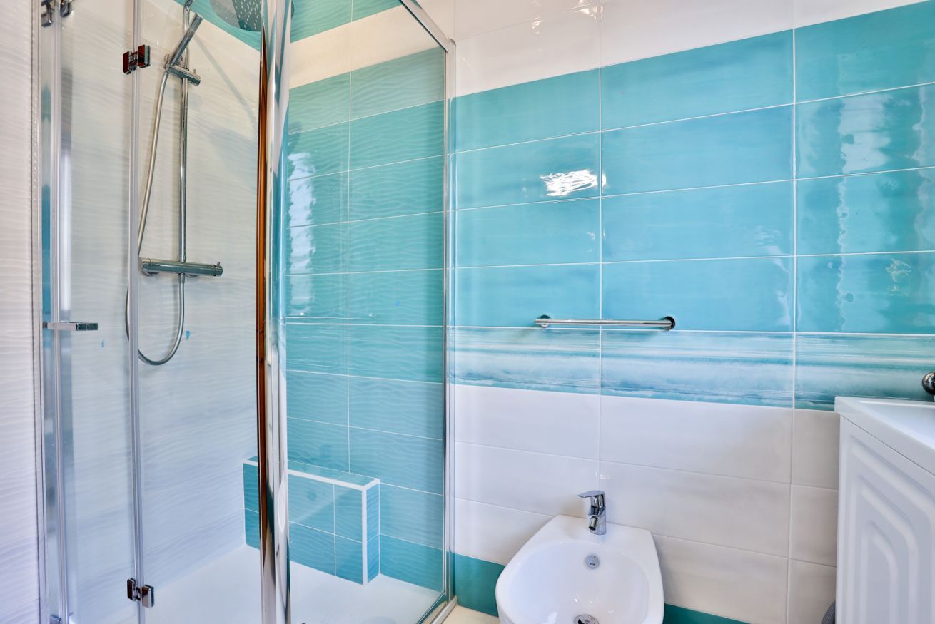 A bathroom with a glass shower enclosure, a white sink, and blue-tiled walls.