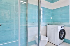 A bathroom with a glass shower enclosure, a toilet, and a washing machine. - GuestHost - Andy's House (Salerno)