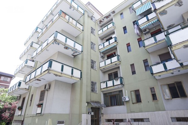 Un immeuble résidentiel à plusieurs étages, doté de balcons, de climatiseurs et d’une entrée sécurisée par un portail.