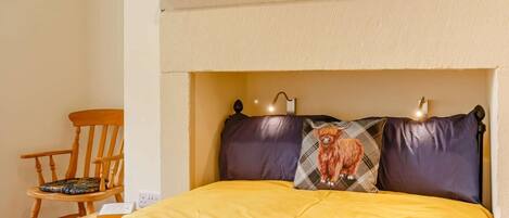 A bed with a yellow blanket, a pillow with a bull design, and a chair with a cushion.