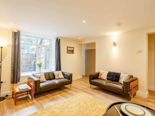 A living room with two leather sofas, a wooden coffee table, a floor lamp, and a large window with curtains. - 2 Bed in Ilkley (oc-89554) (Ilkley)