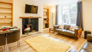 A living room with a fireplace, a sofa, a TV, and a dining area. - 2 Bed in Ilkley (oc-89554) (Ilkley)