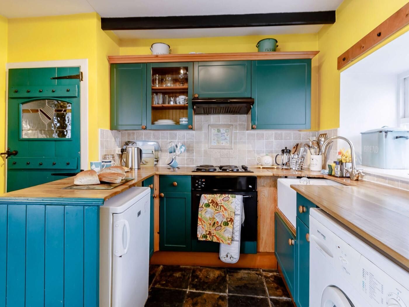 Une cuisine avec des meubles de couleur turquoise, un lave-linge, une cuisinière et un évier.