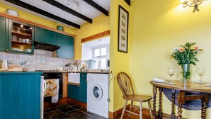 A kitchen with teal cabinets, a washing machine, a dining table with chairs, and a vase with flowers. - 2 Bed in Montrose (oc-an48m) (Johnshaven)