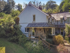 A two-story house with a stone foundation, a covered porch, and a wooden staircase leading to the entrance. - 1 Bed in Newton Abbot (oc-bbell) (Hennock)