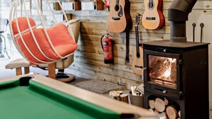 Ein Billardtisch, ein Hängesessel und ein Kaminofen in einem Raum mit Holzwänden und Gitarren.