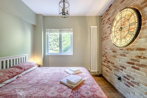 A bedroom with a bed, a window, a radiator, and a brick wall with a clock. - 1 Bed in Newton Abbot (oc-bbell) (Hennock)