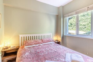 Een slaapkamer met een bed, nachtkastjes en een raam met uitzicht op groen.