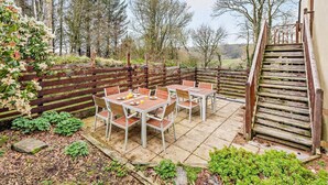 Une terrasse avec une table et des chaises, une clôture en bois et un escalier menant à un niveau supérieur.