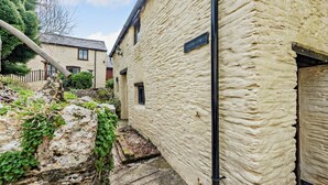 Une ruelle étroite aux murs de pierre, avec une poutre en bois, et une maison dont on aperçoit la fenêtre et la porte.