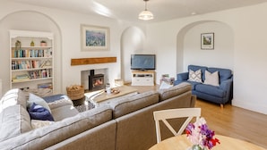 Una sala de estar con chimenea, sofá, televisor, estantería y una zona de comedor con mesa y sillas.