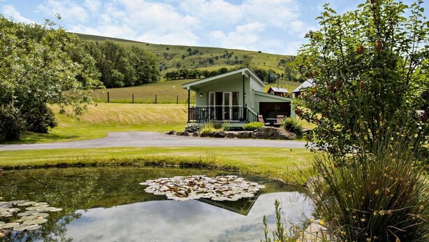 Une maison avec un porche, un étang parsemé de nénuphars et un paysage verdoyant.