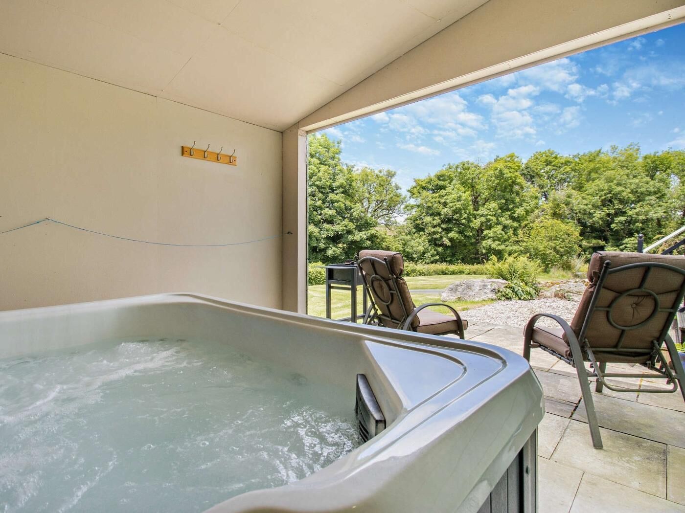 Een hottub met stoelen, een houten kapstok en uitzicht op een groen landschap.