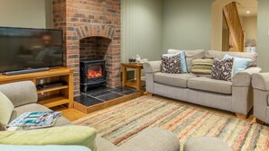 Ein Wohnzimmer mit Kamin aus Backsteinen, einem Fernseher, einer Couch und einem gemusterten Teppich.