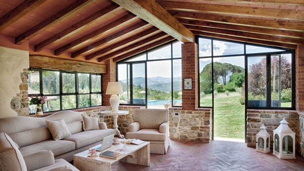 Um quarto aconchegante com lareira de pedra, um sofá, uma poltrona e uma grande janela com vista para o exterior.