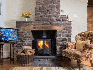 A stone fireplace with a television on a wooden table, a wicker basket, and a patterned armchair. - 1 Bed in Crickhowell (oc-bn079) (Llangynidr)