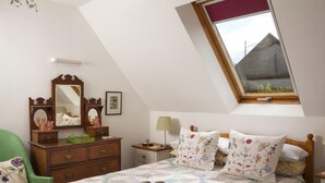 Ein Schlafzimmer mit schrägen Wänden, einer Holzkommode, einem Bett mit floralem Bettbezug und einem Oberlicht.