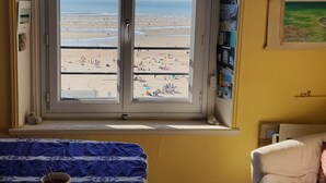 Ein Zimmer mit einem großen Fenster mit Blick auf einen Strand, ein kleiner Tisch mit einer Tasse und ein Stuhl.