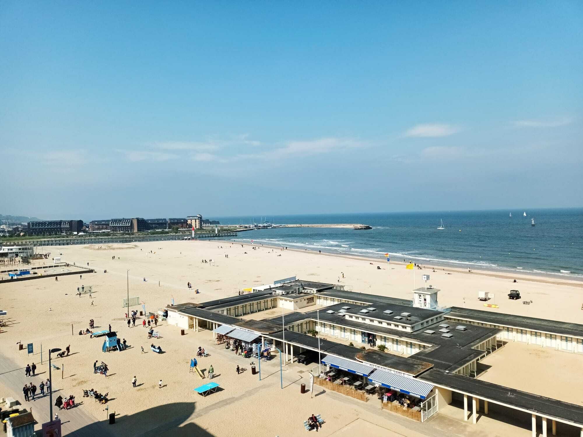A beach with a boardwalk, beach umbrellas, and a building with a sign.