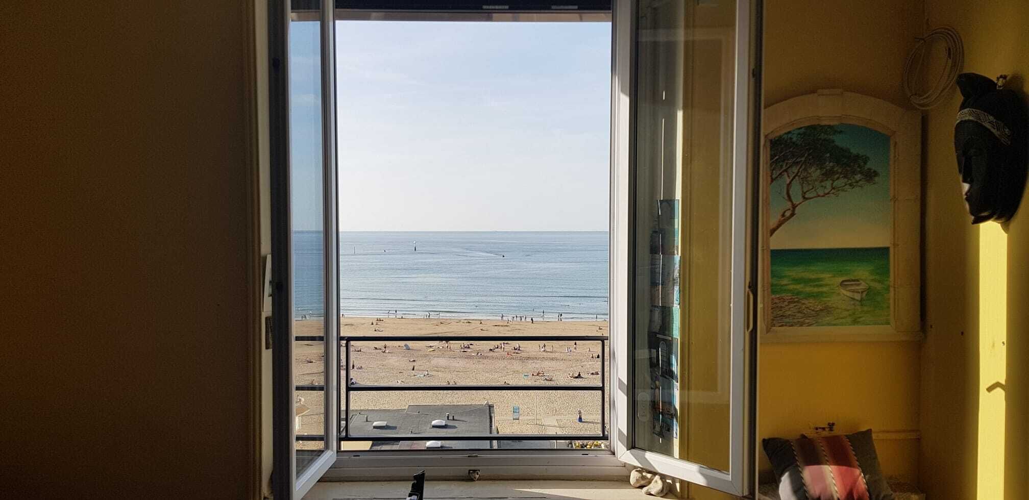 Une pièce avec vue sur la plage et l’océan, accessible par une porte ouverte.