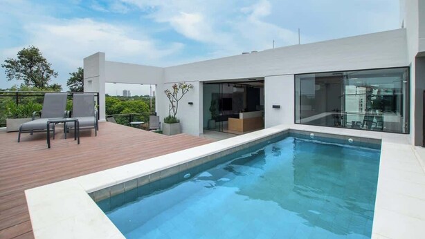 A modern outdoor swimming pool with a wooden deck, glass doors, and a view of the city. - Corporate Stays Insignia City - A44 (Asunción)