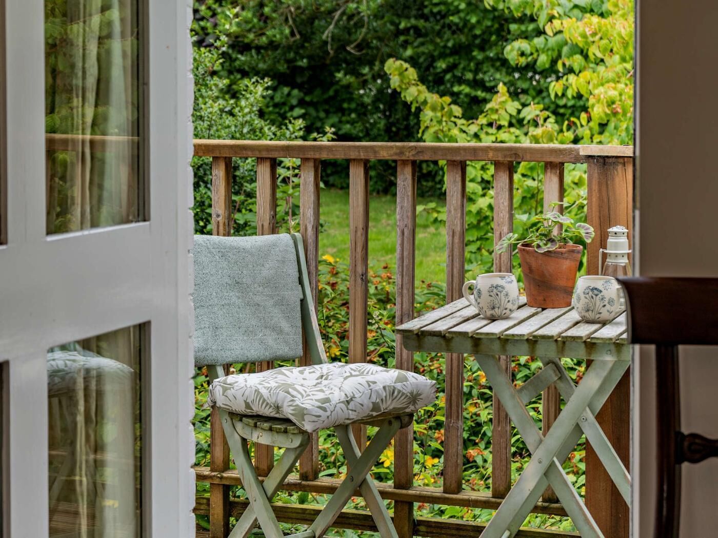 A wooden deck with a cushioned chair and a small table, a potted plant, and a candle holder.