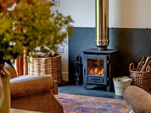 A cozy living room with a wood-burning stove, wicker baskets, and a patterned rug. - 1 Bed in Brecon (oc-bn157) (Llanfihangel Tal-y-llyn)