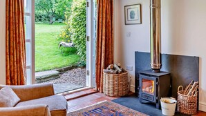 Ein gemütliches Zimmer mit Kamin, einer Couch, einem Teppich und Blick auf einen Garten.