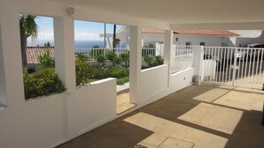 Ein überdachter Außenbereich mit Blick auf das Meer, weißen Wänden und einem verschlossenen Eingang.
