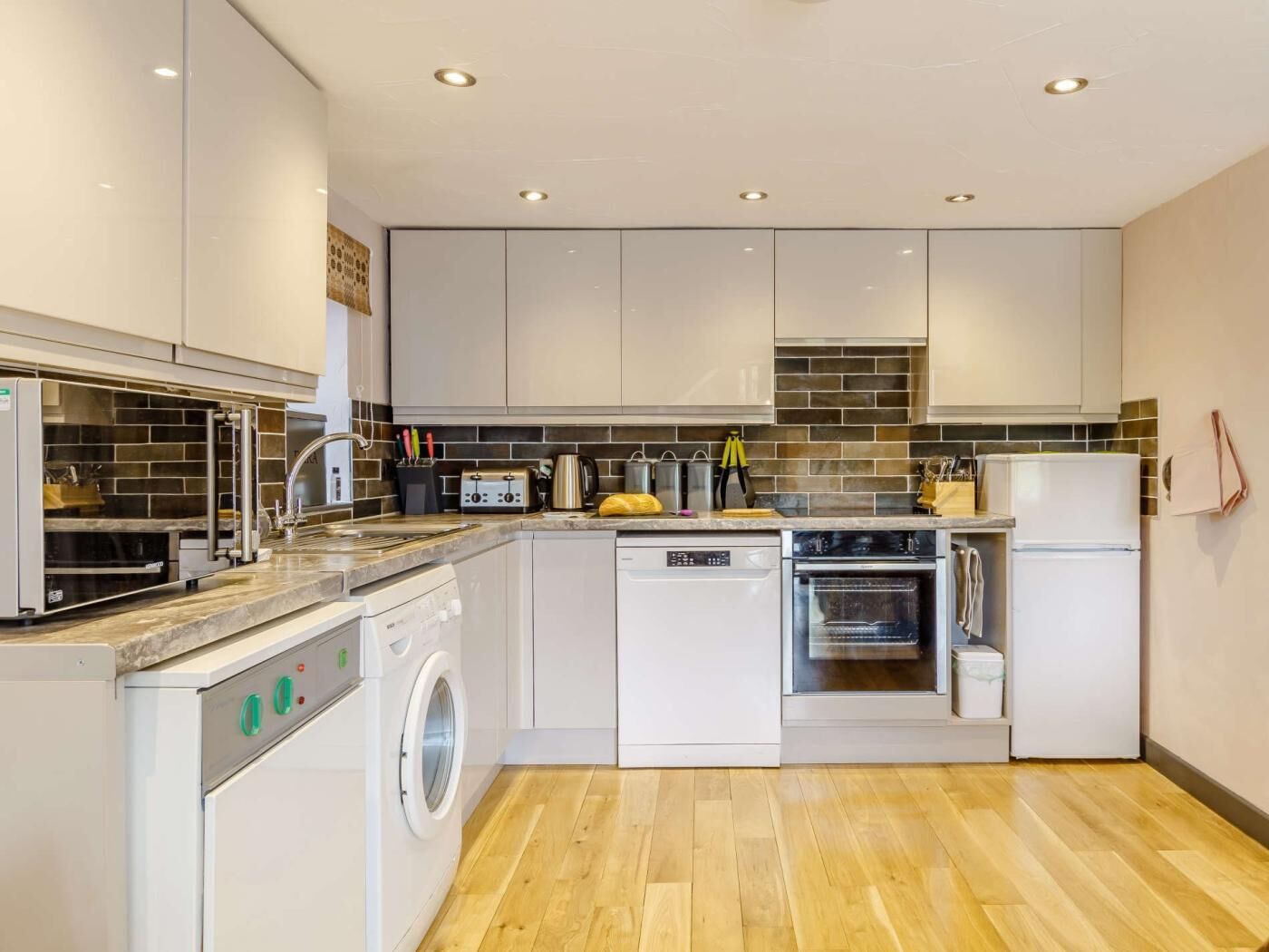A modern kitchen with white cabinetry, a built-in dishwasher, an oven, and a washing machine.