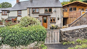 A two-story house with a stone facade, a wooden front door, and a visible satellite dish. - 2 Bed in Brecon (oc-bn138) (Bwlch)