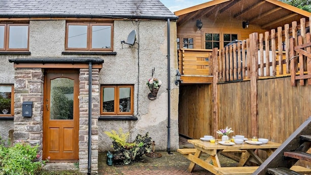 A rustic cottage with a stone facade, wooden door, and a small garden area with a picnic table set up. - 2 Bed in Brecon (oc-bn138) (Bwlch)