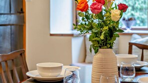 A dining table set with white plates, bowls, and glasses, a vase with flowers, and a window in the background. - 2 Bed in Brecon (oc-bn138) (Bwlch)